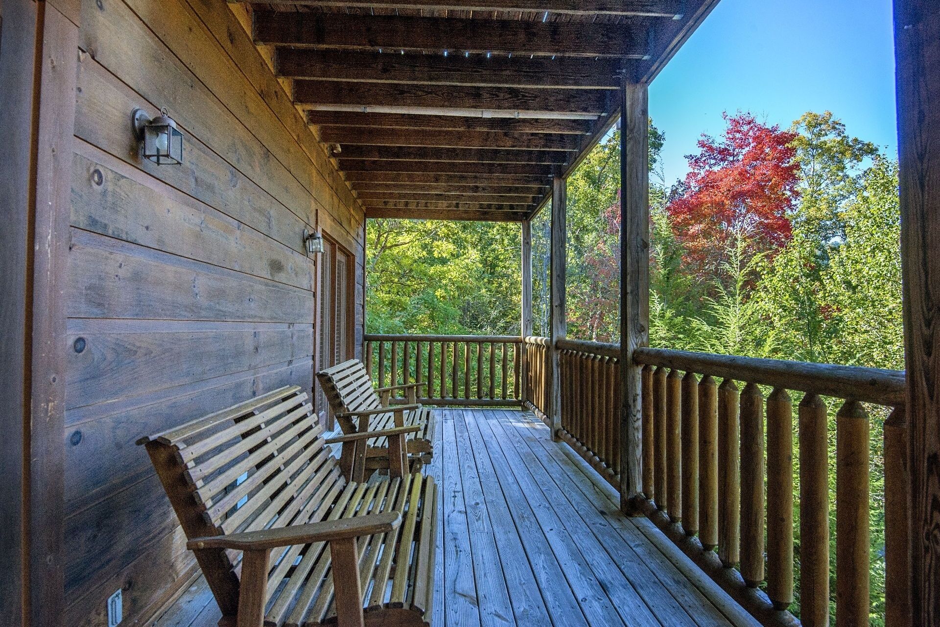 A wooden porch with two benches and a railing overlooking a forested area with autumn foliage.