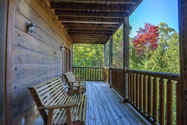 A wooden porch with two benches and a railing overlooking a forested area with autumn foliage.