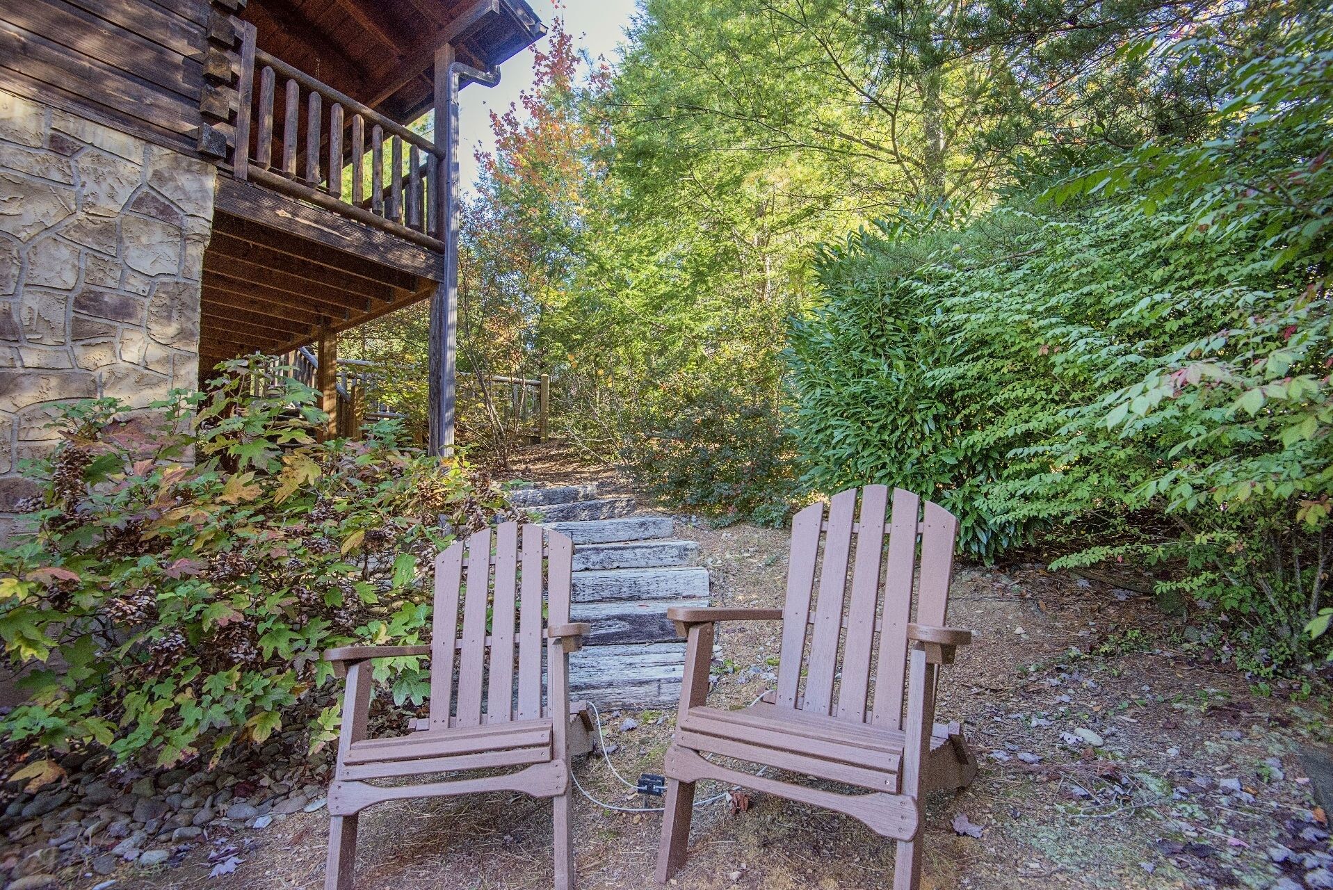 Two Adirondack chairs in a forested area with a stone building in the background.