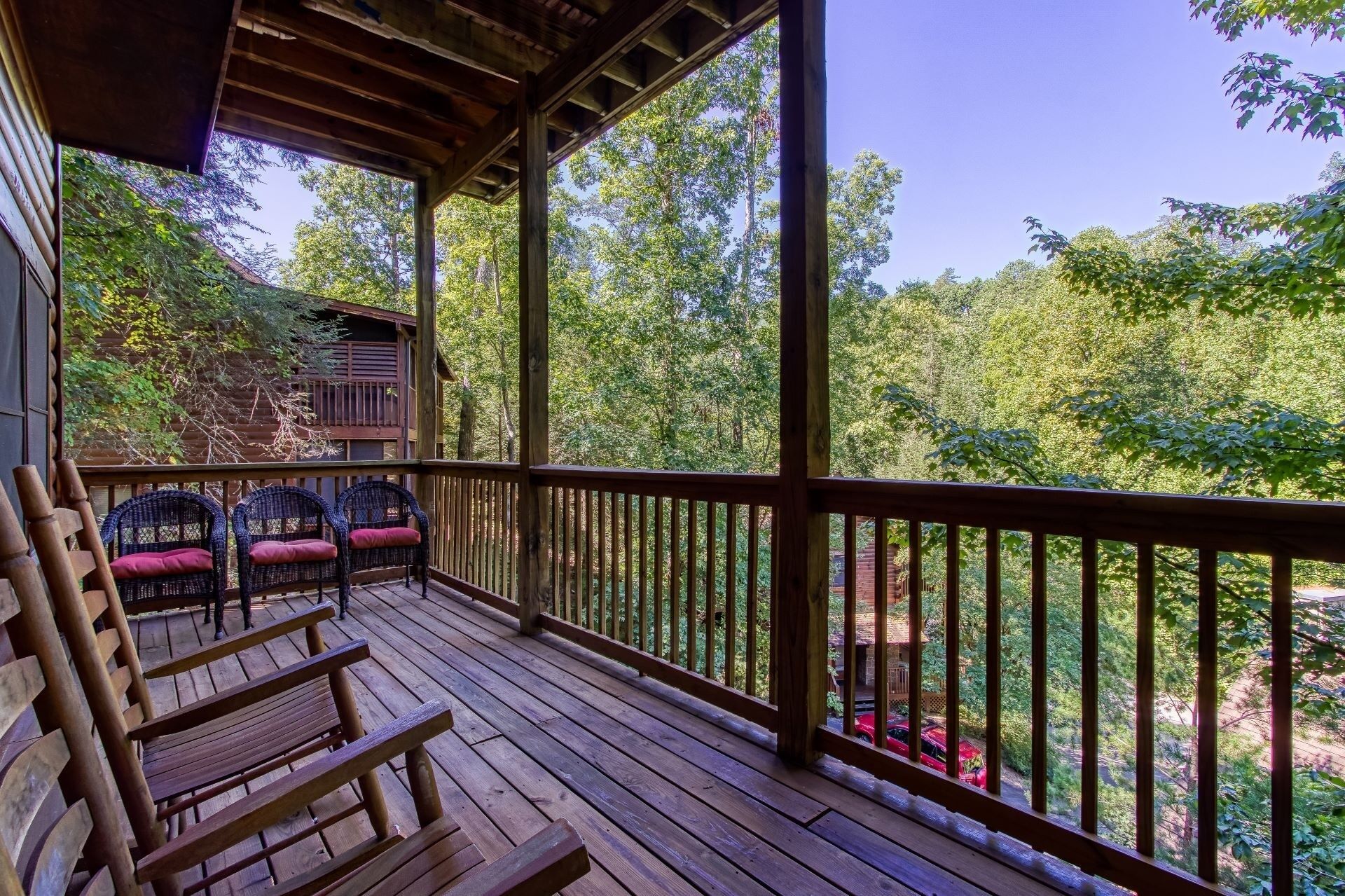 A wooden deck with wicker chairs and a view of a forest.