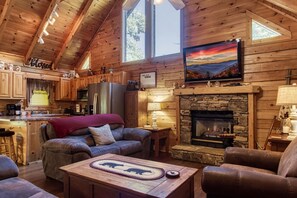 A cozy cabin interior with a stone fireplace, wooden furniture, and a kitchen area. - ER222 - Al's Nest - Great Location - Close To Town! 2 Bedroom Cabin by RedAwning (Pigeon Forge)