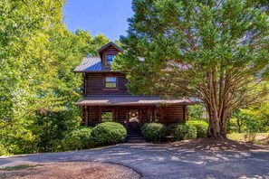 A log cabin with a steeply pitched roof, a front porch, and a driveway leading to the entrance.