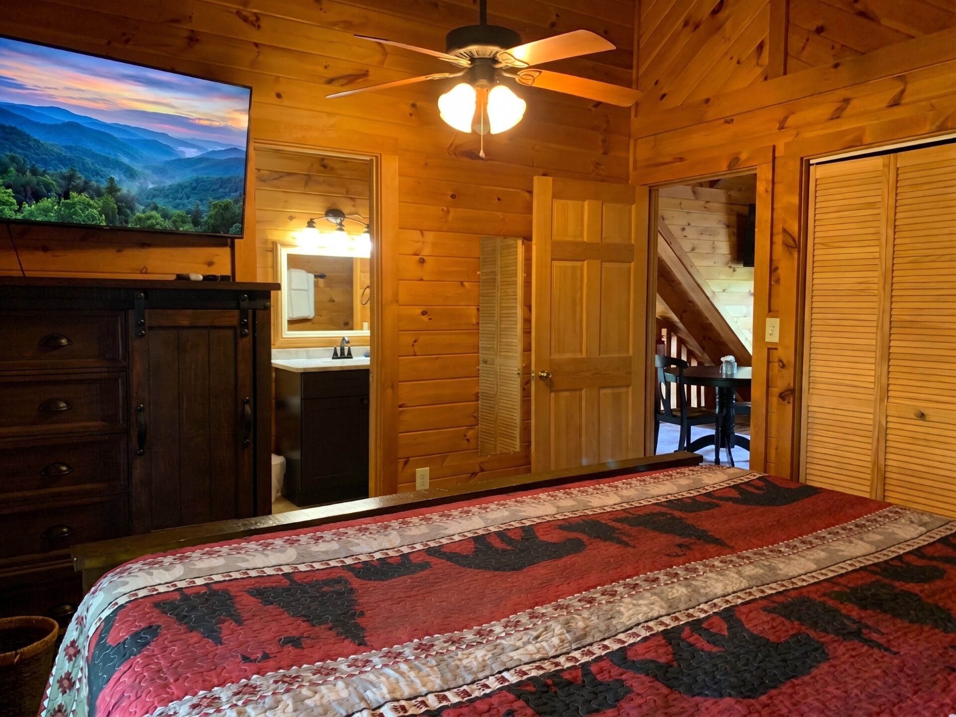 A wooden cabin bedroom with a bed, dresser, and a ceiling fan.