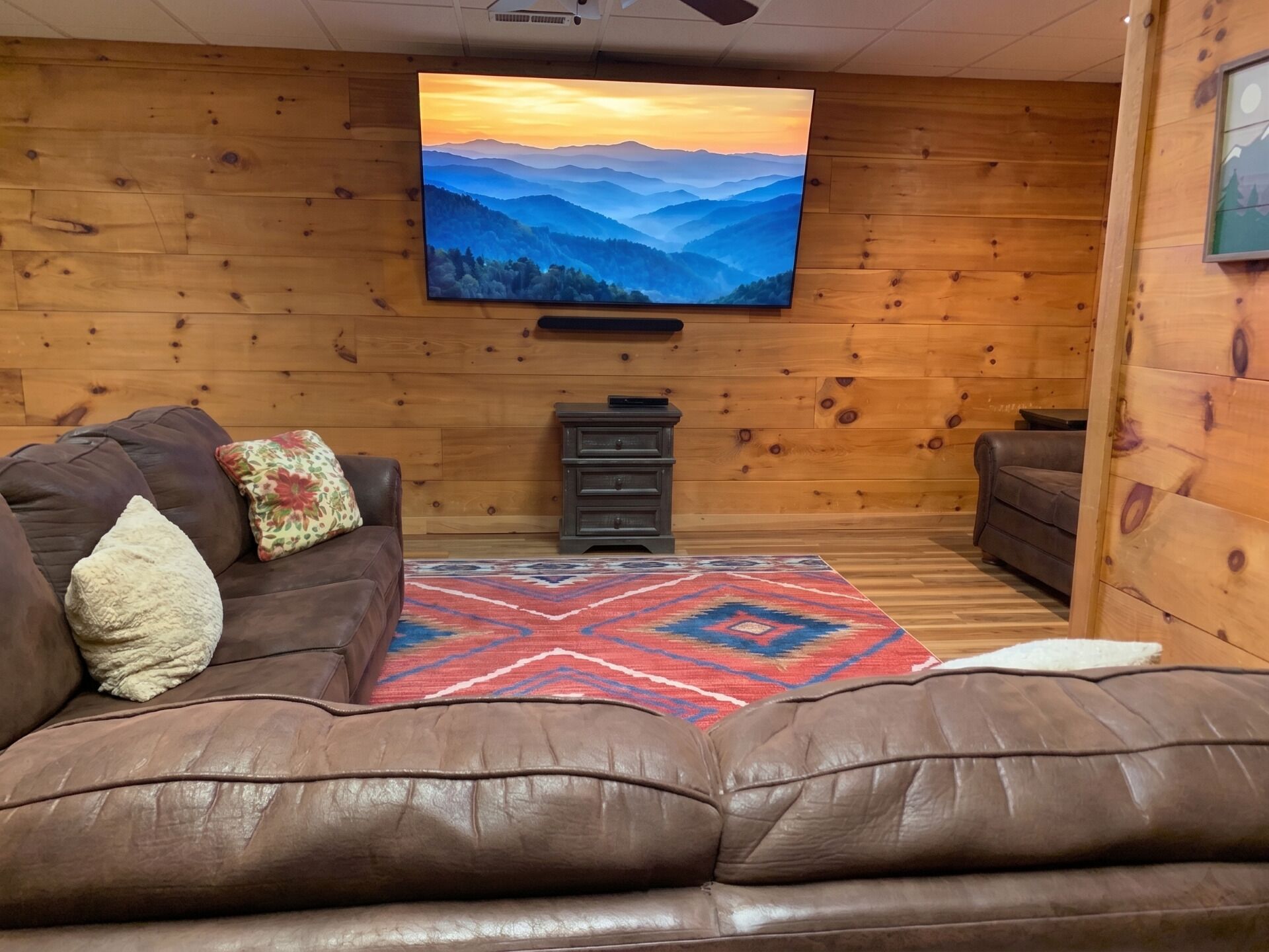 A cozy living room with a leather couch, a TV mounted on the wall, and a patterned rug.