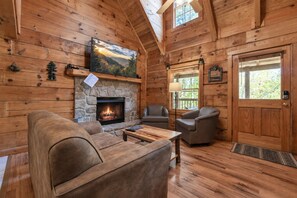 A cozy cabin interior with a stone fireplace, leather furniture, and wooden walls.