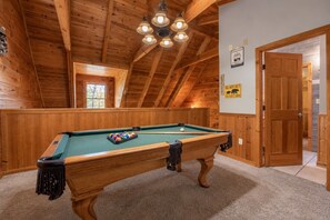 Een pooltafel in een houten kamer met een schuine kap en een deur aan de rechterkant.