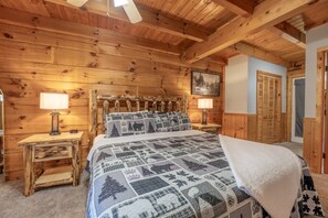Een slaapkamer in een houten blokhut met een bed, twee nachtkastjes en een plafondventilator.