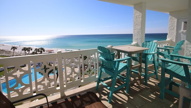Un balcon avec des chaises turquoise et une table donnant sur une plage et l’océan.
