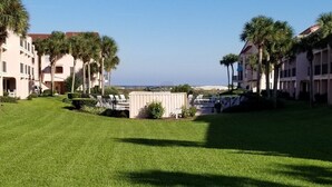 A hotel courtyard with a well-maintained lawn, palm trees, and a pool area. - Sea Place 13137 2 Bedroom Condo by RedAwning (St. Augustine)