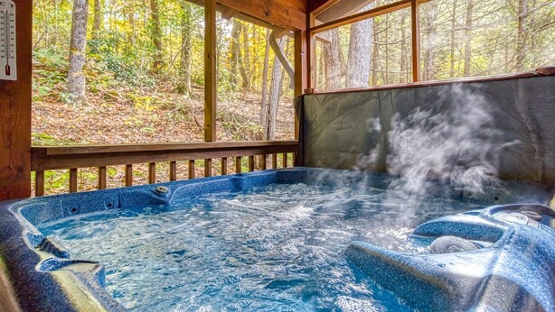 A hot tub with steam rising, surrounded by wooden deck and forest views. - Er202 - Now And Forever Great Location! - Close To Town! 4 Bedroom Cabin by RedAwning (Pigeon Forge)