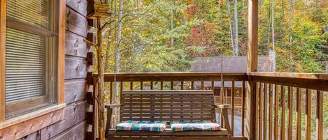 A wooden porch with a bench, a window, and a view of a forest.