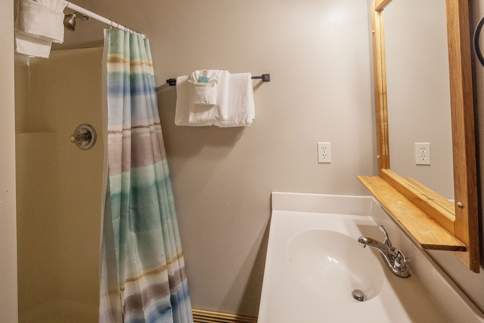 Un baño con ducha, lavamanos, espejo y toallero.