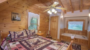 Interior de cabana com uma cama, janela com vista, ventoinha no teto e porta de madeira.