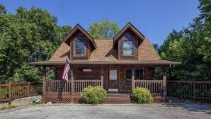 A wooden cabin with a porch, two chimneys, and an American flag.