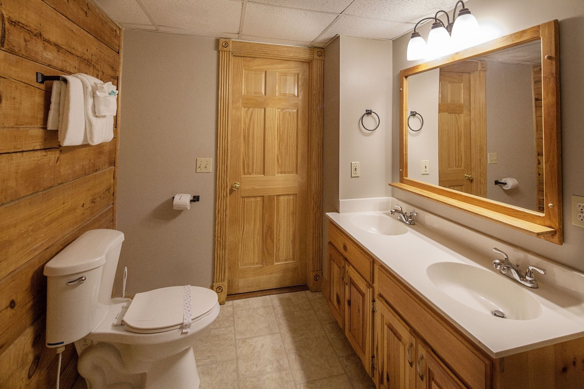 A bathroom with wooden walls, a toilet, a sink, and a mirror.