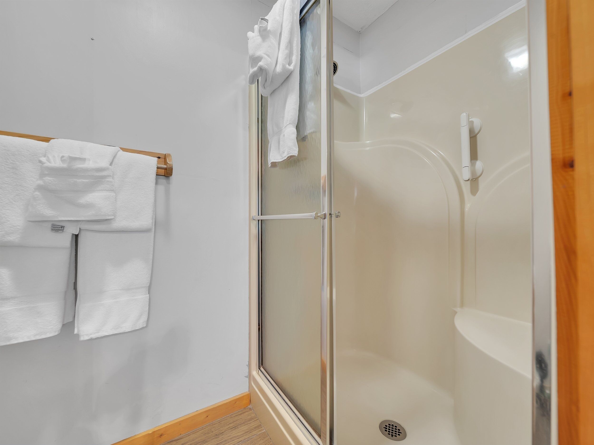 Une douche avec une porte en verre, un sol en bois et un porte-serviettes avec des serviettes pliées.