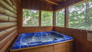 A wooden cabin with a hot tub and large windows overlooking a forest. - Er65 - Eagles Point - Great Location. Close To All The Action! 2 Bedroom Cabin by RedAwning (Pigeon Forge)