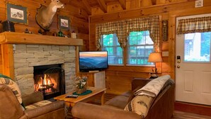A cozy cabin interior with a stone fireplace, leather furniture, a mounted deer head, and a television. - Er65 - Eagles Point - Great Location. Close To All The Action! 2 Bedroom Cabin by RedAwning (Pigeon Forge)