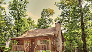 A rustic log cabin with a stone chimney, wooden porch, and a small staircase leading to the entrance. - Er65 - Eagles Point - Great Location. Close To All The Action! 2 Bedroom Cabin by RedAwning (Pigeon Forge)