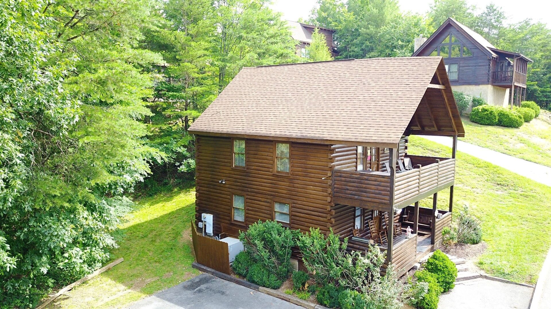 A wooden cabin with a balcony, surrounded by lush greenery.