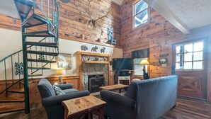 A cozy cabin interior with a wooden staircase, a fireplace, a television, and a sofa. - Er13 - Moose Manor Great Location - Close To Town! 3 Bedroom Cabin by RedAwning (Pigeon Forge)