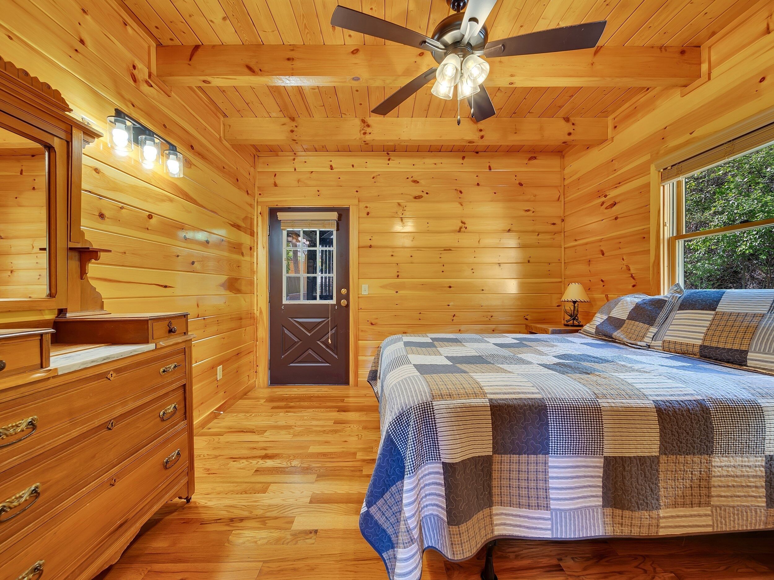 A wooden cabin bedroom with a bed, dresser, and ceiling fan.