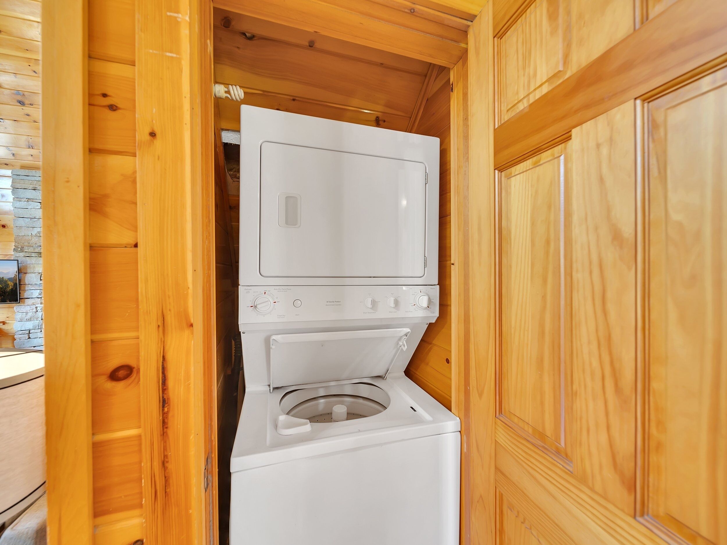 A laundry room with a stacked washer and dryer, wooden walls, and a stone wall with a picture.