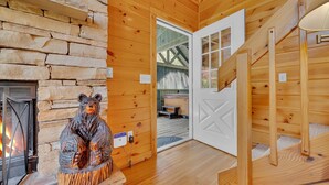 A cozy cabin interior with a stone fireplace, a wooden bear sculpture, and a wooden staircase. - Tranquility - Quiet And Comfortable Cabin! Close To The Tanger Outlet Shopping 2 Bedroom Cabin by RedAwning (Sevierville)