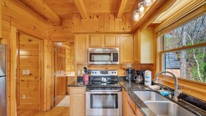 A wooden cabin kitchen with a stainless steel stove, microwave, and sink. - Tranquility - Quiet And Comfortable Cabin! Close To The Tanger Outlet Shopping 2 Bedroom Cabin by RedAwning (Sevierville)