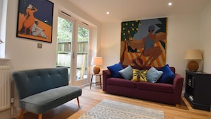 A living room with a blue sofa, a purple sofa with multiple cushions, a patterned rug, a painting on the wall, and a lamp on a side table. - Southbank (Rye)