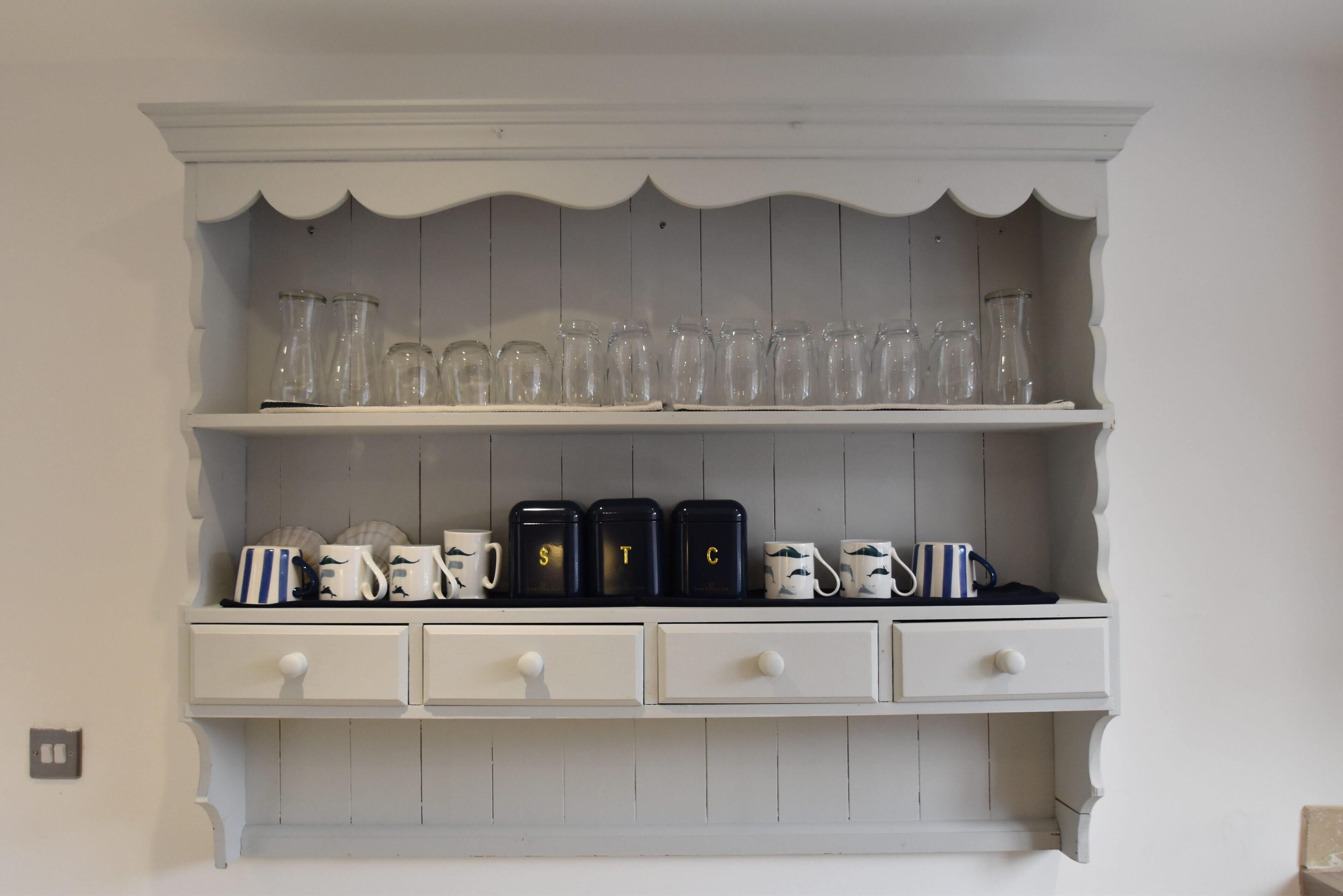 A white wooden shelf with glass jars and black containers.