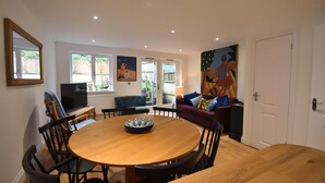 A dining area with a round wooden table, black chairs, and a television on a stand. - Southbank (Rye)