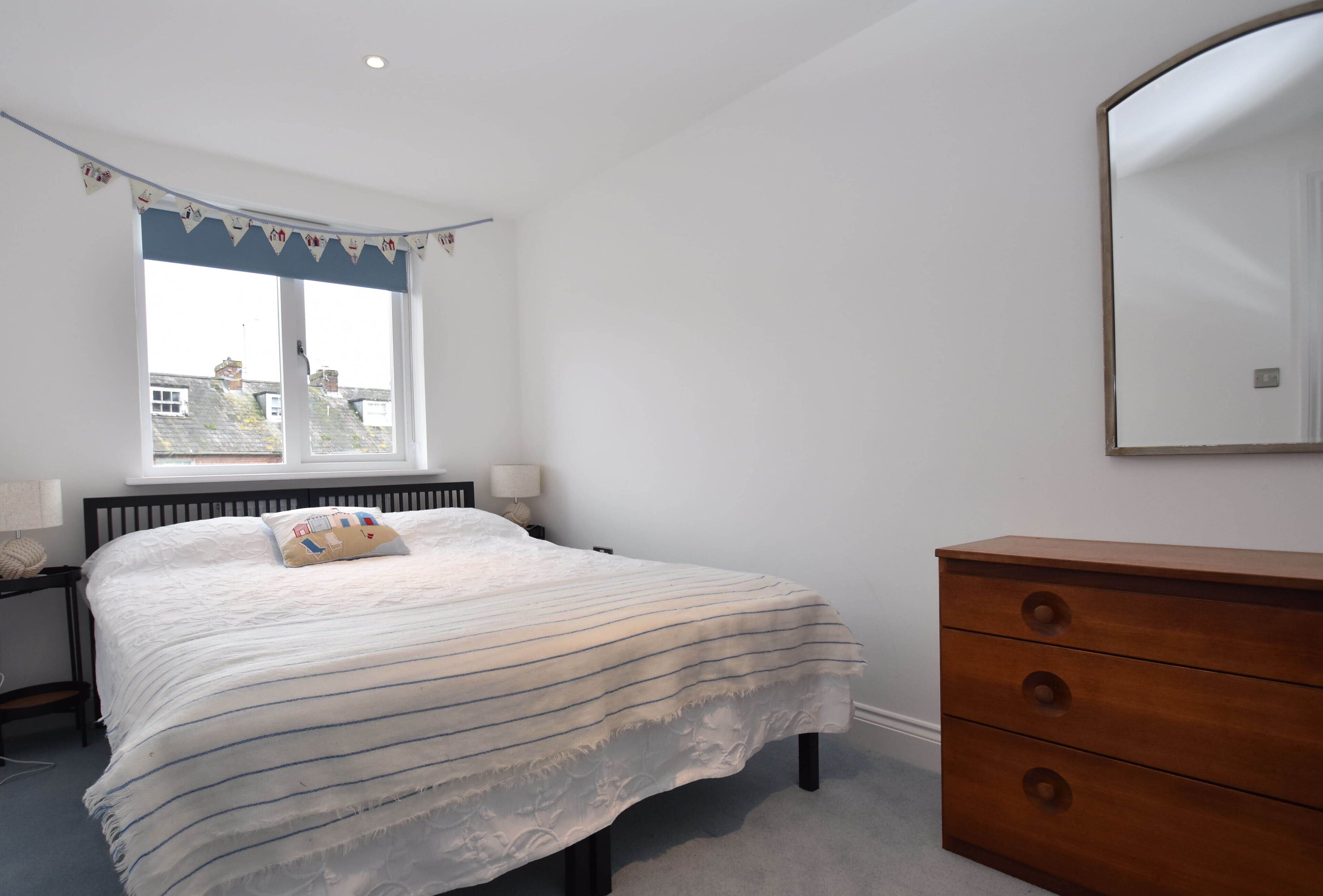 Une chambre à coucher avec un lit, une commode, une fenêtre et un miroir.