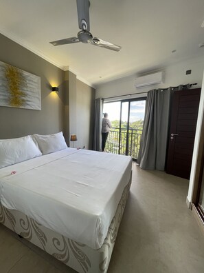 Quarto de hotel com uma cama grande, um ventilador de teto, uma luminária na parede e uma varanda com vista.
