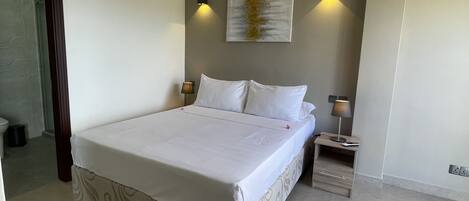 Ein Schlafzimmer mit einem großen Bett, einem Deckenventilator, einem Nachttisch mit Lampe und einer Wandleuchte.