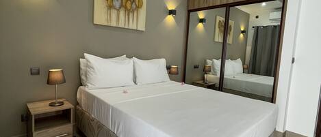 A bedroom with a large bed, a ceiling fan, a nightstand with a lamp, a wall-mounted artwork, and a mirror.