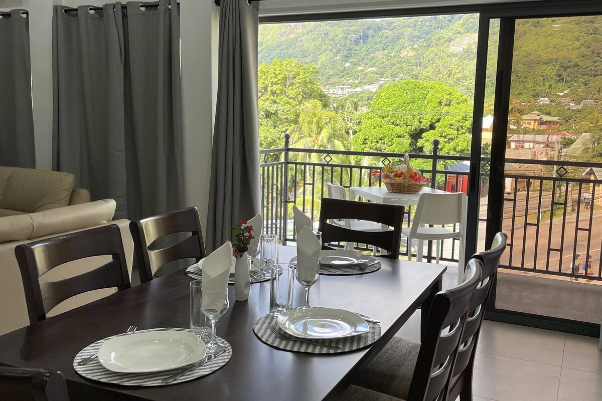 A dining area with a table set for four, chairs, and a view of a lush landscape through large windows.