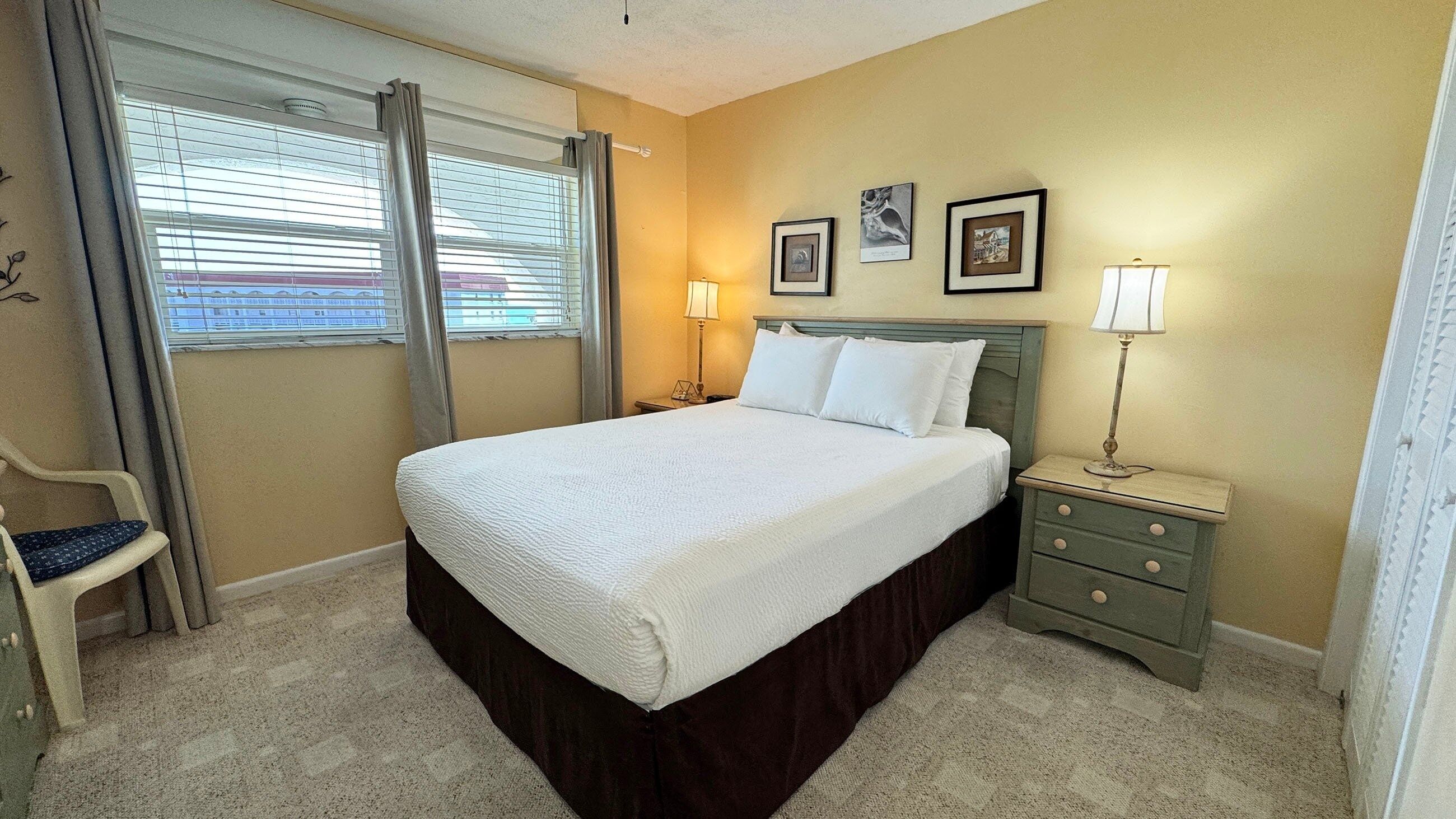 A hotel room with a bed, two bedside tables, a chair, and a window with blinds.