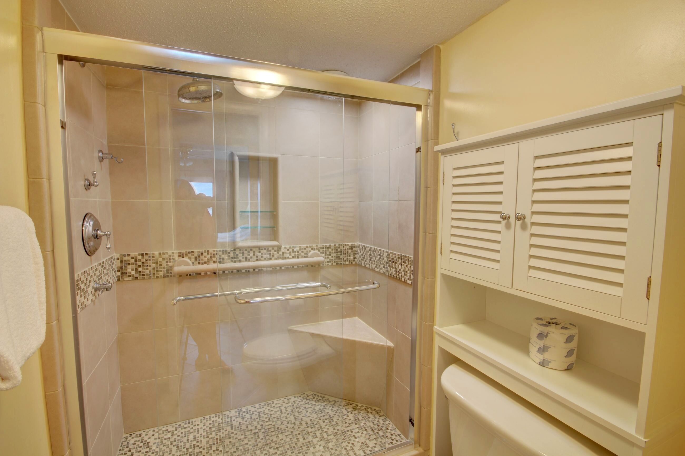A walk-in shower with a glass door, a toilet, and a shelf with toiletries.