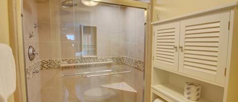 A walk-in shower with a glass door, a toilet, and a shelf with toiletries.