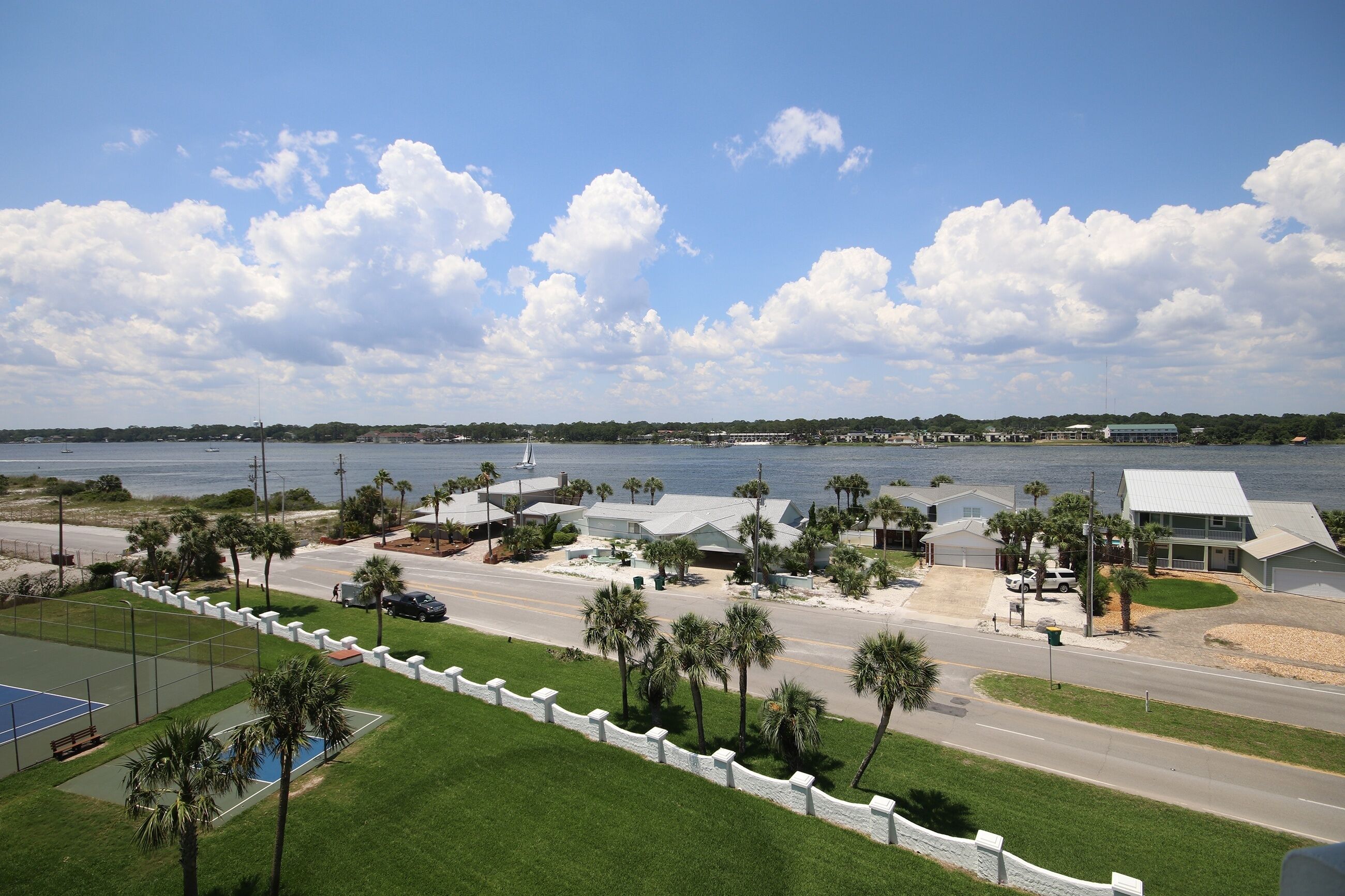 A coastal property with a road leading to a beach, a tennis court, and a view of the ocean.