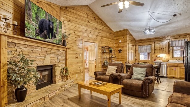 Interior acogedor de una cabaña de troncos con chimenea, mobiliario de cuero, televisor y una zona de cocina.