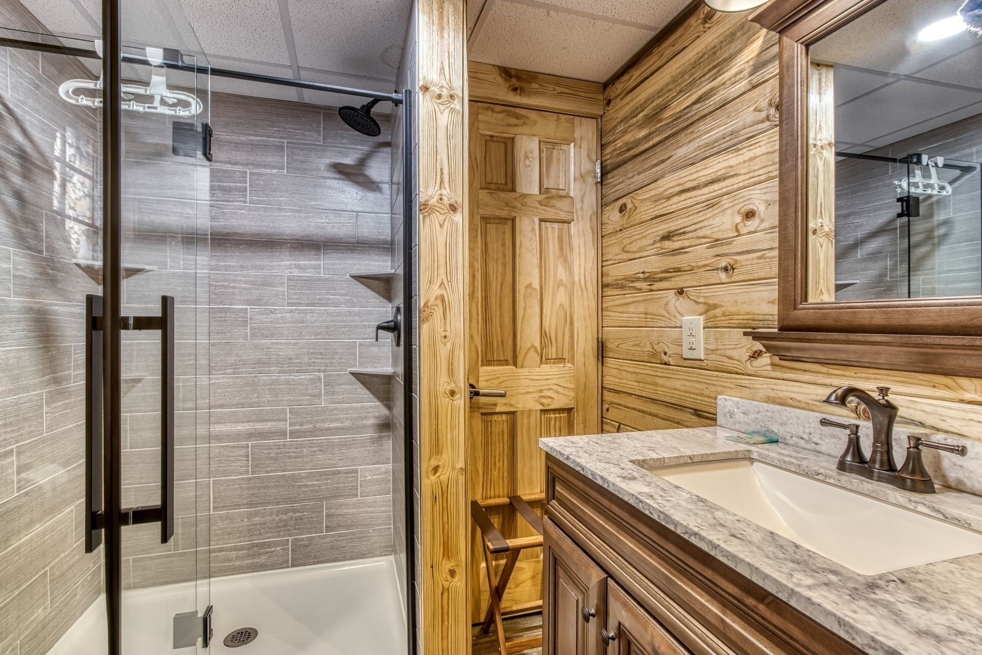 A bathroom with a glass shower enclosure, a wooden door, and a marble sink with a mirror.