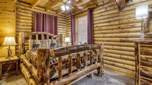Un dormitorio de cabaña con una cama de madera rústica, un ventilador de techo y un televisor montado en la pared.