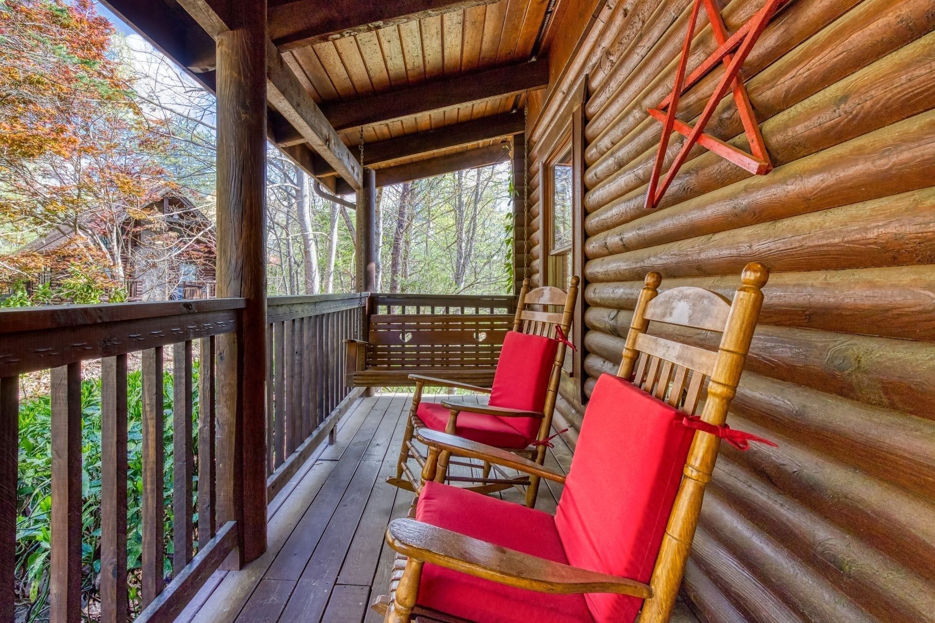 A wooden log cabin with a porch featuring two red cushioned rocking chairs and a wooden ladder.