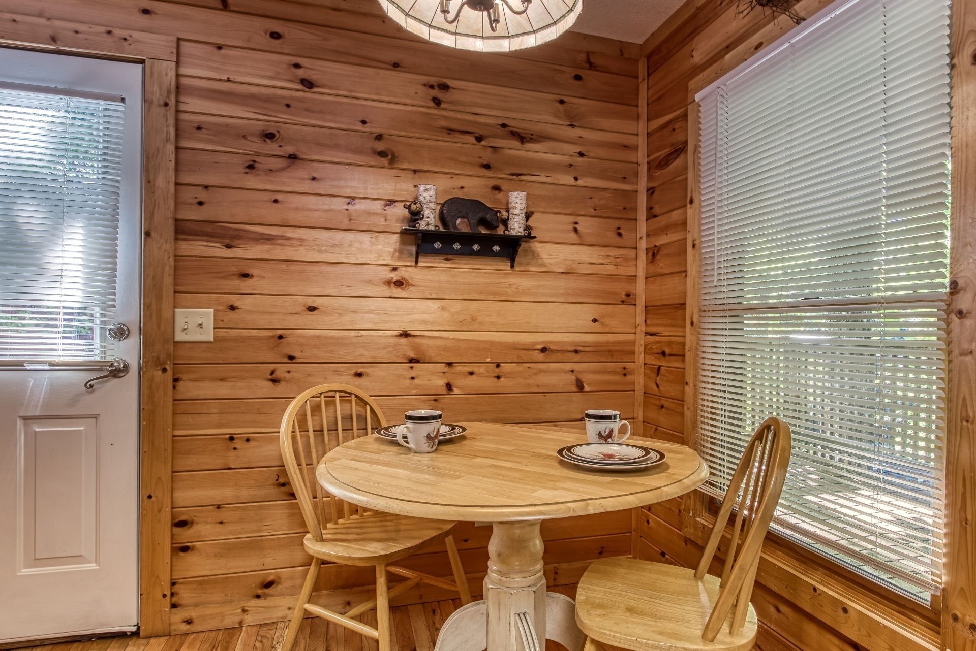 Un intérieur en bois avec une table ronde et des chaises, une porte et une fenêtre avec des stores.
