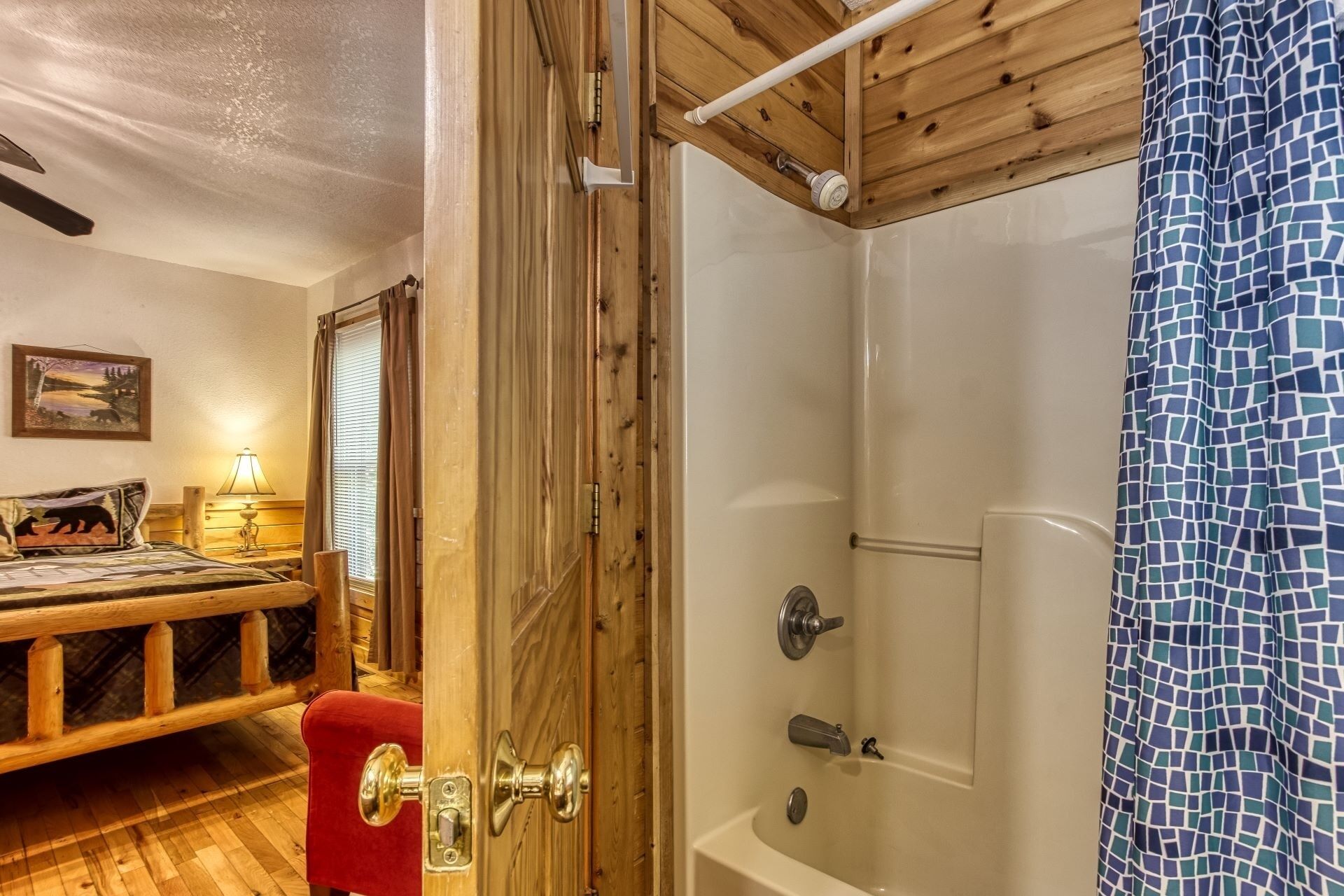 Une pièce aux murs en bois, comprenant un lit, une table de chevet, une lampe et une douche avec un rideau de douche en mosaïque bleue.