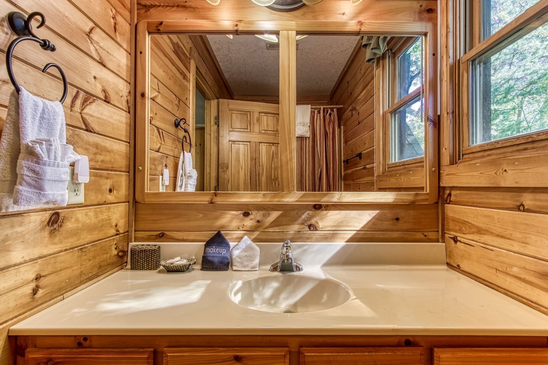 Baño de cabaña de madera con un espejo grande, un lavamanos y armarios de madera.