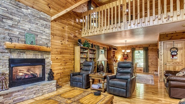 A cozy log cabin interior with a stone fireplace, leather sofas, and a wooden coffee table. - Whispering Oaks - Private Pigeon Forge Getaway...close To Tanger Outlet Shopping 2 Bedroom Cabin by RedAwning (Sevierville)
