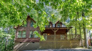 A log cabin with a balcony, surrounded by dense forest. - Whispering Oaks - Private Pigeon Forge Getaway...close To Tanger Outlet Shopping 2 Bedroom Cabin by RedAwning (Sevierville)